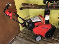 Full view of red and black snowblower on wooden pallet