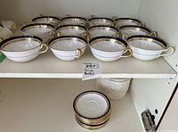 Multiple white soup bowls with cobalt blue and gold rims arranged on a shelf, stack of matching saucers below