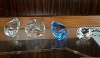 Four Swarovski crystal pieces including two clear balls, one blue heart, and one clear heart placed on a reflective surface.