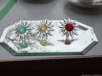 Three Swarovski crystal flowers with blue, yellow, and red centers on a beveled mirror base.