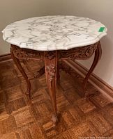 Front angled view of square side table showing beveled marble top and carved floral wood legs and frame.