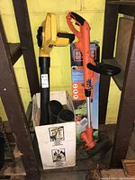 Photo showing Black+Decker electric edge trimmer GH900 standing upright next to boxed Paramount leaf blower PB300C with visible branding and controls.