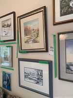 Photo showing two framed watercolor paintings by Nora Gross hung on wall, depicting nature landscape scenes.