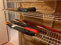 Nine umbrellas of various lengths and designs on a metal rack in a wooden room, showing different handle styles and color patterns.