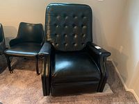 Front view of vintage black leather easy chair rocker with button tufted backrest and armrests, sitting next to a small black chair.