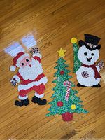 Full set of three plastic popcorn Christmas decorations on wooden floor: Santa Claus, Christmas tree with detached star, and snowman.