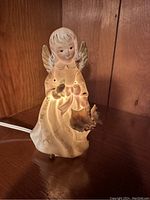 Front view of the ceramic angel light, showing face, wings, and basket with small flower.