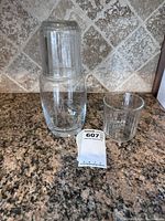 Bedside water carafe filled with water with one glass stacked on top and one glass next to it on granite countertop, showing etched monogram and glass details.