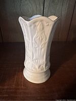 Front view of white glazed Belleek Galway Irish pottery vase with detailed raised floral patterns and scalloped top edge