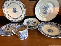 Six assorted blue and white china pieces on wooden surface, including various plates and a mug.