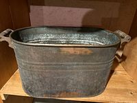 Side view of a rectangular copper bucket with wooden handles showing aged and worn patina.