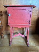 Front view of the red painted wooden humidor cabinet with copper lining and white enamel knob, showing decorative molding on the door and curved stand legs.