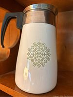 Photo of the white coffee pot with green avocado medallion design, black handle, and stainless steel rim.