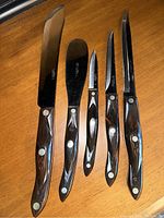 Photo showing all five knives and cutlery utensils with black marbled handles and riveted construction.