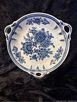 Top view of round Delft Blue serving plate with three handles and central blue floral handpainted design on white ceramic.