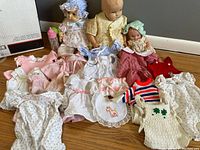 Three baby dolls with assorted baby doll clothes and a baby bottle displayed on the floor.