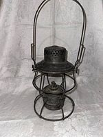 Front view of the antique railroad lantern showcasing the wire cage, oil reservoir, and handle.