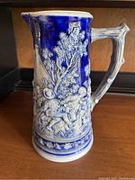 Front view showing detailed relief of people and dog, deep cobalt blue background.