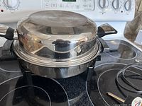 Closed stainless steel electric skillet with lid on stovetop, showing handles and overall condition.