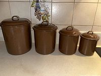 Set of 4 brown speckled enamelware canisters with lids arranged from largest to smallest on countertop.
