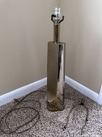 Full view of the tall modernist silver metal lamp showing its form, metal finish, and included cords.