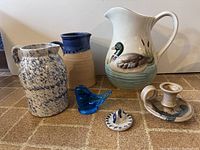 Photo showing all items including three pitchers, blue art glass bird, candlestick holder and cookie mold, arranged on a tiled surface.