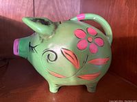 Side view of the bright green piggy bank with pink snout and floral patterns on the body.