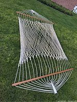 Full view of the rope hammock unfolded on a lawn, showing open weave cotton or polyester rope and one wooden spreader bar at one end.