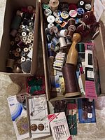 Overall view showing multiple boxes filled with various sewing threads, bobbins, hand sewing needles, pins and clips.