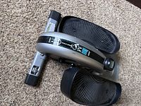 Top view of the compact elliptical strider showing textured foot pedals, central resistance knob, and base supports with safety information labels.