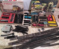 TYCO and Athearn HO scale train sets with their original boxes, locomotives, freight cars, track pieces, and Kaybee power supply displayed on a table.