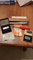 Overview of all items on a wooden table including Zippo pocket cutter in case, 2-in-1 letter opener and screwdriver tool, red-handled screwdriver with packaging and documents.