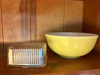Clear glass rectangular butter dish with ribbed vertical lines and matching lid with lifting tab, displayed on wooden shelf.
