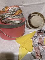 Overview of the lot showing the Christian Dior turban hat on the pink round hat box, yellow scarf, patterned scarf, and straw garden party hat.