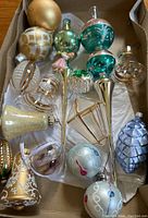 Overhead view of assorted vintage glass ornaments in a box showing multiple shapes and colors including finials, balls, and bells.