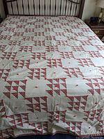 Full view of vintage quilt laid out on bed showing geometric patchwork pattern in red floral triangles and white blocks.