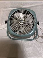 Front view of vintage Lasko enamel fan showing metal grille, logo, blades, and stand.