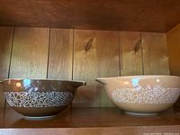 Two vintage Pyrex mixing bowls, brown and beige, showing the Woodland white floral pattern around the exterior. Both bowls have pouring spouts and molded handles. Photo shows the exterior side view.