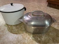 Photo showing the white enamelware stock pot with lid and the Wagner Ware Magnalite Roasterette side by side on kitchen floor.