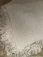 Close-up view of the white chenille fabric and twisted fringe on the bedspread corner to show texture and fringe detail.