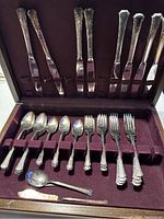 Full view of flatware set inside box showing knives, spoons, forks, and spreader arranged neatly.