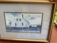 Framed watercolor style print showing a white house with chimney and windows, signed by Andrew Wyeth, with gold frame and double matting, taken from front angle.