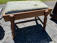 Front side view of antique solid wood footstool showing the upholstered removable top and turned wood legs.
