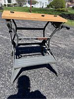 Front view of workmate portable work center showing the wooden work surface, vise clamps, metal frame, and footrest.
