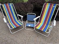 Photo showing two adult beach chairs with multicolor vertical striped fabric and one child-sized beach chair with blue horizontal striped fabric, all with white metal frames.
