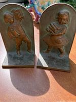 Pair of brass bookends with patina, showing boy and girl relief designs carrying books.