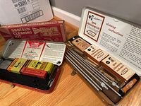 Photo showing multiple gun cleaning kits in metal cases and cardboard boxes, including cleaning rods and solvent packages.