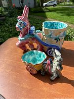 Front view of two ceramic donkey planters on a table, larger with pink and blue accents and smaller in grey and yellow.