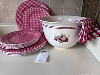 Photo showing melamine gingham check plates stacked in front of a large Pfaltzgraff mixing bowl with apple motif, with a kitchen towel draped over the bowl.