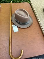 Photo showing both the tipped wooden cane and the fedora hat on a brown leather surface.